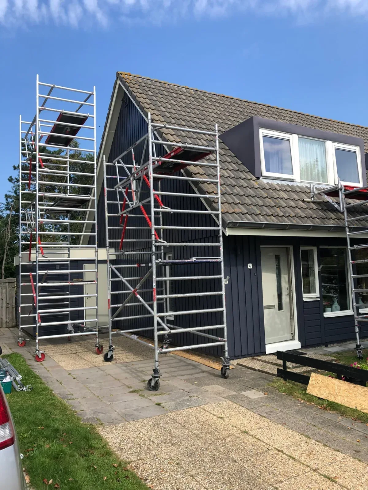 Steigerwerk rondom een donkerblauwe houten woning tijdens buitenschilderwerk